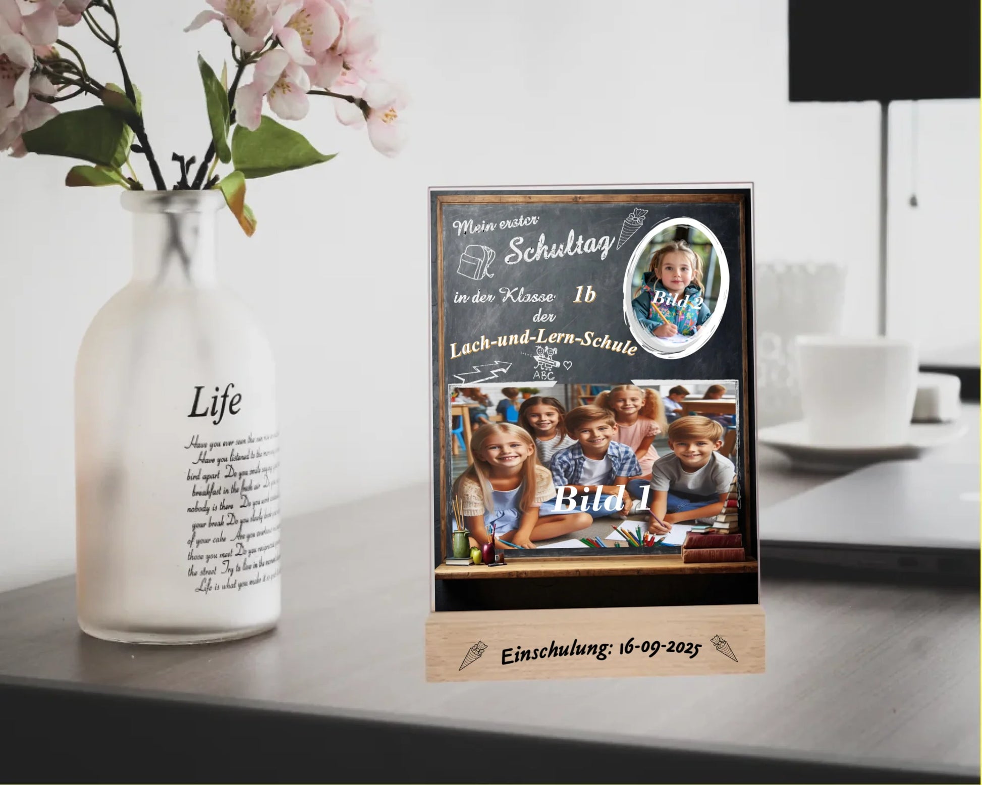 personalisierte-erinnerungstafel-15x20cm-aus-acrylglas-mit-2-fotos-name-der-schule-und-der-klasse-hintergrund-schultafel-bedruckt-mit-echtholz-standfuß-graviert-mit-einschulungsdatum-erinnerungstafel-steht-auf-einem schreibisch-neben-einer-vase-mit-blume