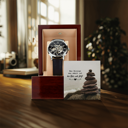 armbanduhr-aus-edelstalhl-mit-schwarzem-lederarmband-und-schwarzen-zifferbaltt-steht-in-einer-holzbox-auf-einem-holztisch-daneben-eine-grußkerte