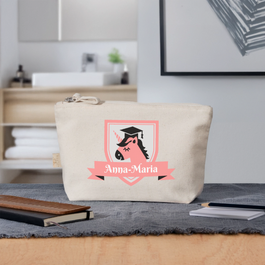federmaeppchen-250x140mm-beige-mit-reissverschluss-pinkes-wappen-mit-einhorn-kopf-darunter-ein-pinker-banner-mit-dem-personalisierten-namen-federmaeppchen-steht-auf-einem-schreibtisch