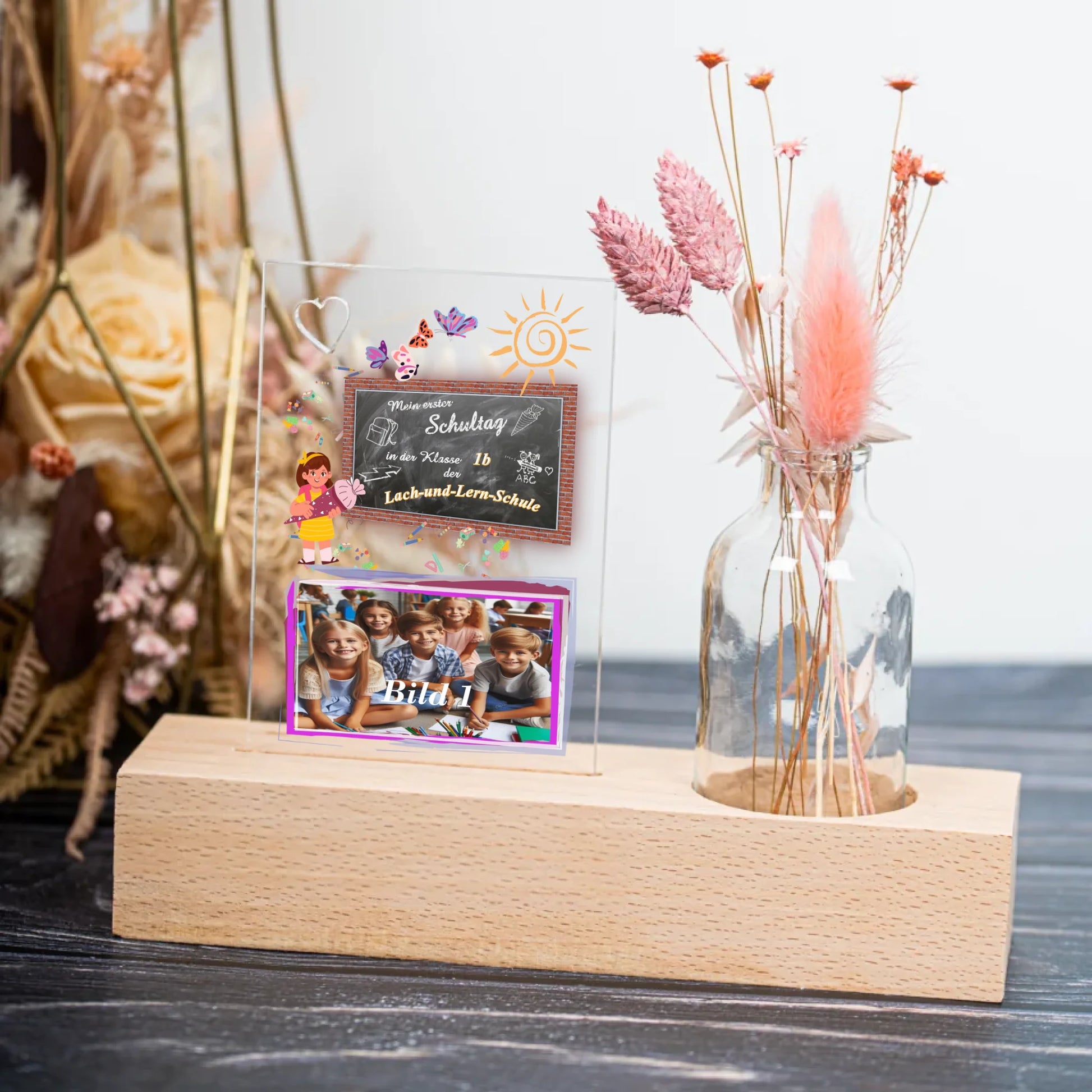 fotoaufsteller-aus-acrylglas-8x11,5cm-personalisiert-mit-foto-und-name-der-schule-mit-kleiner-vase-mit-trockenblumen-auf-einem-hellen-echtholz-sockel-fotoaufsteller-stehtauf-einer-schwarzen-tischplatte