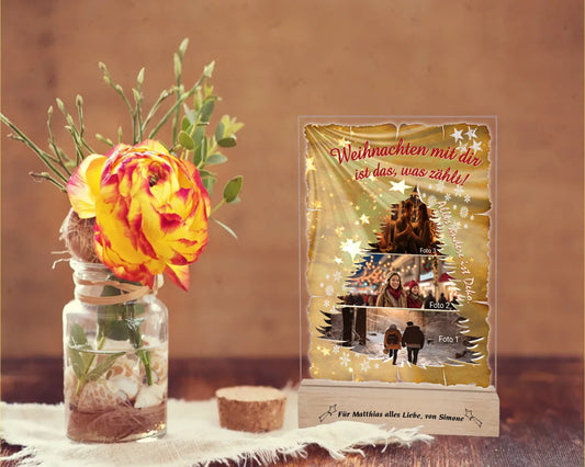 fotoaufsteller-acryl-15x20cm-mit-graviertem-standfuss-acrylglas-mit-3-teiliger-foto-collage-in-tannenbaum-form-darueber-schriftzug-weihnachten-mit-dir-ist-das-was-zaehlt-und-neben-der-collage-steht-alles-andere-ist-deko-mit-einem-hintergrund-optik-goldenes-papier-mit-sternen-und-schneeflocken-fotoaufsteller-steht-auf-rustikalem-holztisch-neben-einer-rose