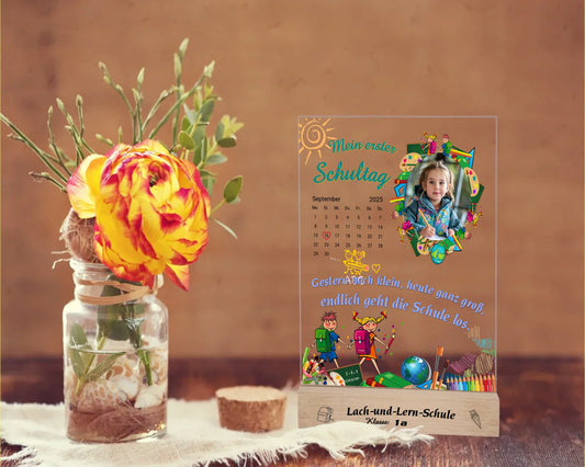 personalisierter-fotoaufsteller-aus-acryl-15x20cm-mit-foto-und-kalenderblatt-zum auswählen-des-datums-zwischen-bunten-schulmotiven-auf-graviertem-holzsockel-mit-name-der-schule-und-der-klasse-fotoaufsteller steht-auf-rustikalem-holztisch-neben-einer-rose