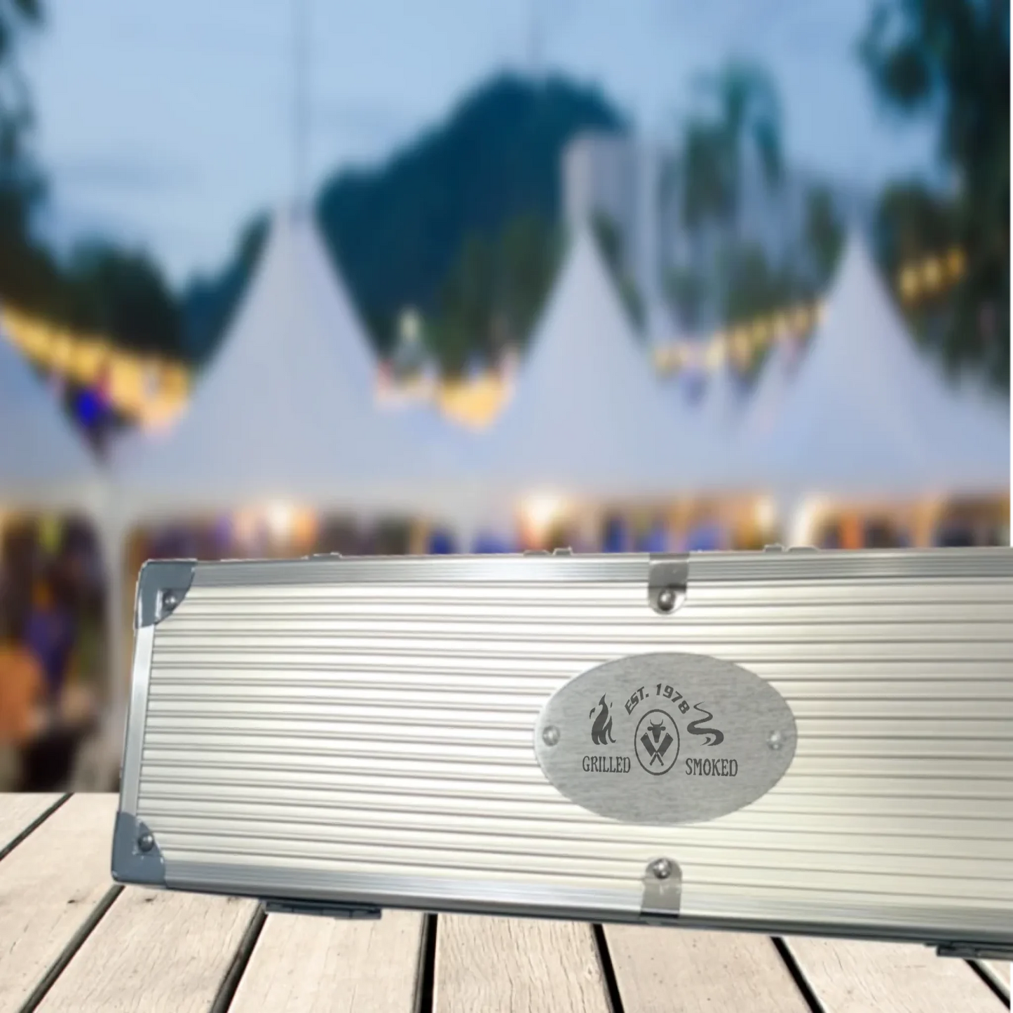 grillkoffer-geschlossen-mit-gravierter-persönlicher-gravur-im hintergrund-sind-pavilions-und-lichter-zu-sehen
