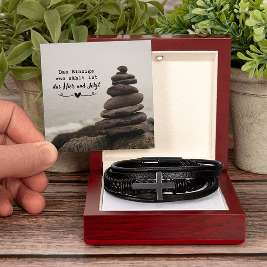 geflochtenes-kunsteder-armband-mit-edelstahl-kreuz-in-schwarzem-finish-in-der-luxusbox-aus-holz-mit-led-darüber-die-karte-mit-gestapelten-steinen-und-botschaft-das-einzige-was-zählt-ist-das-hier-und-jetzt