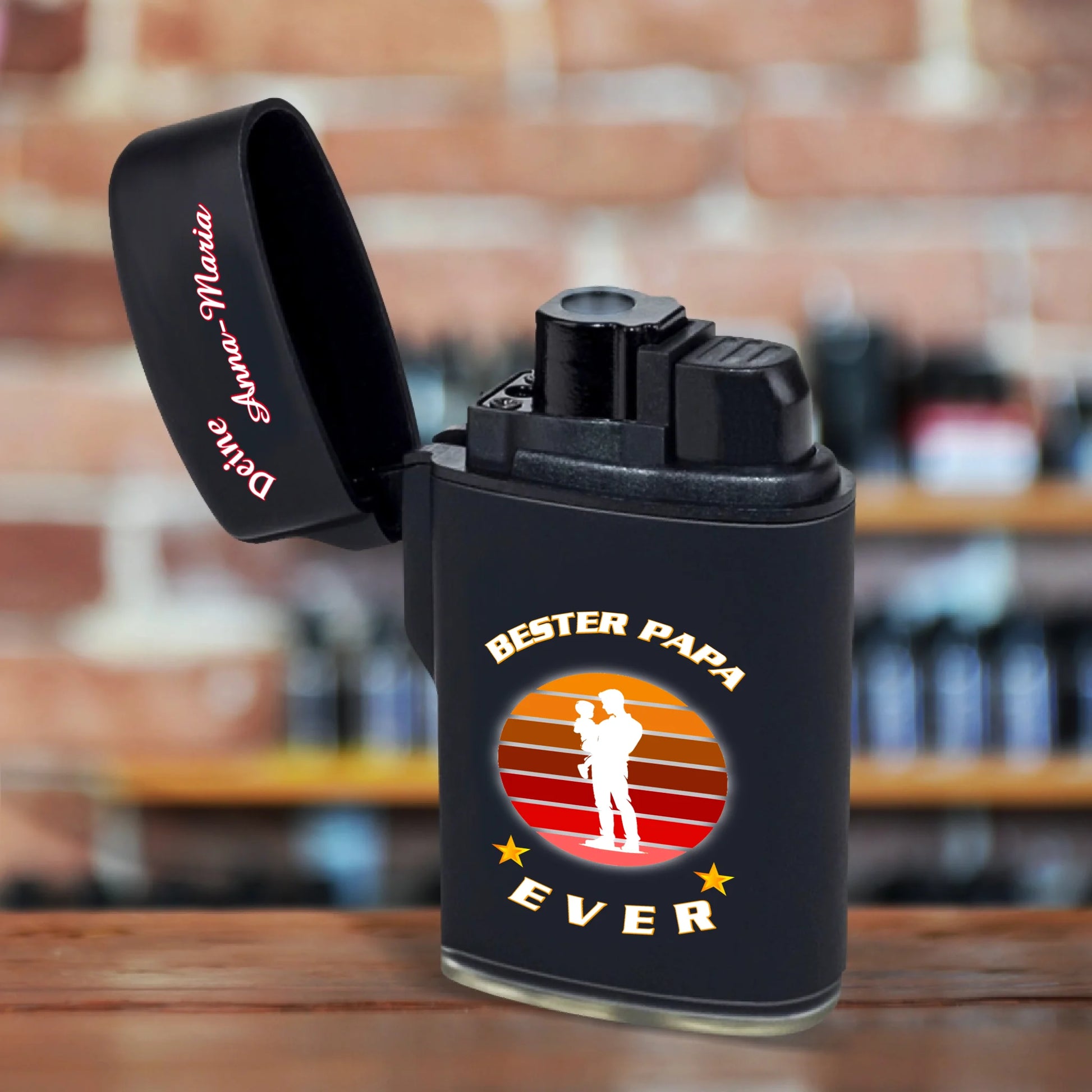 feuerzeug-schwarz-mit-deckel-geoeffnet-mit-beschriftung-bester-papa-ever-in-weiß-und-silhouette-vater-mit-kind-auf-dem-arm-feuerzeug-steht-auf-rustikalem-holztisch
