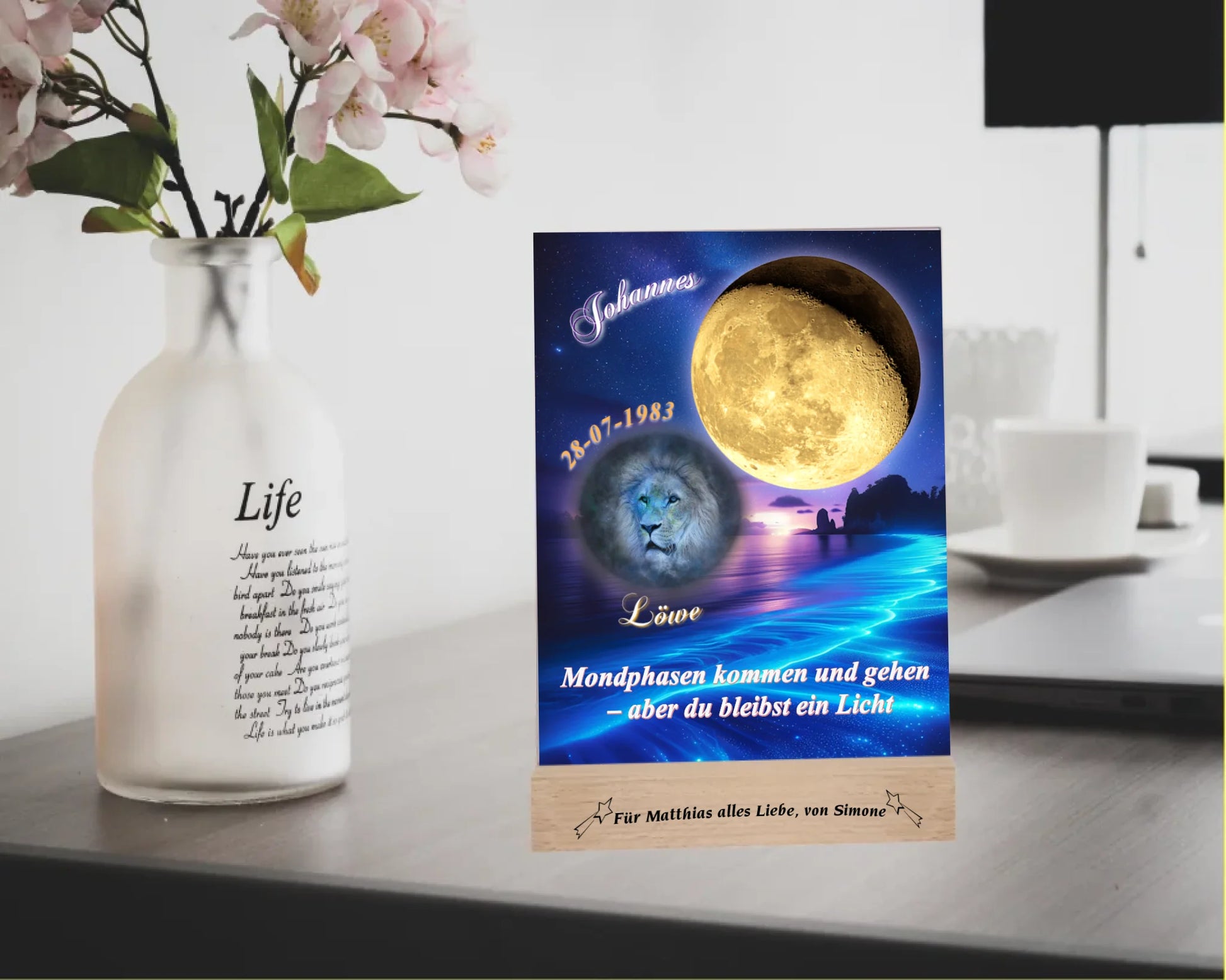 acrylglas-15x20cm-mit-graviertem-holzsockel-design-mit-personalisierter-mondphase-nach-datum-mit-sternzeichen-und-name-kurzer-spruch-monphasen-kommen-und-gehen-aber-du-bleibst-ein-licht-designhintergrund-brandung-meer-in-neon-blau-sternzeichen-ist-hellblau-dargestellt-und-der-mond-golden-acrylglas-steht-auf-schreibtisch-neben-einer-vase-mit-blumen