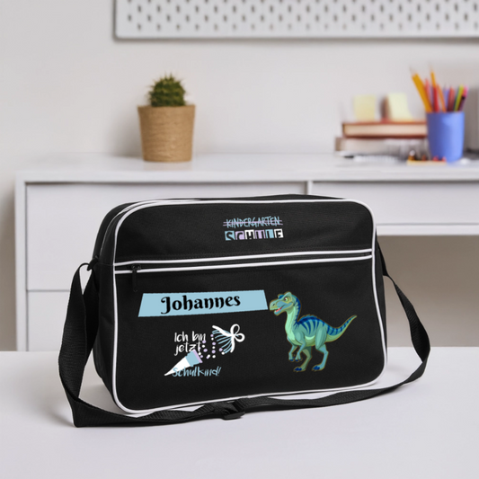 umhaengetasche-40x28cm-schwarz-mit-weissen-kontraststreifen-mit-2-reissverschluessen-und-umhaengegurt-design-dinosaurier-in-blau-gruen-plus-schultuete-mit-schriftzug-ich-bin-jetzt-ein-schulkind-daneben-der-personalisierte-name-auf-hellblauem-banner-tasche-steht-auf-einem-schreibtisch