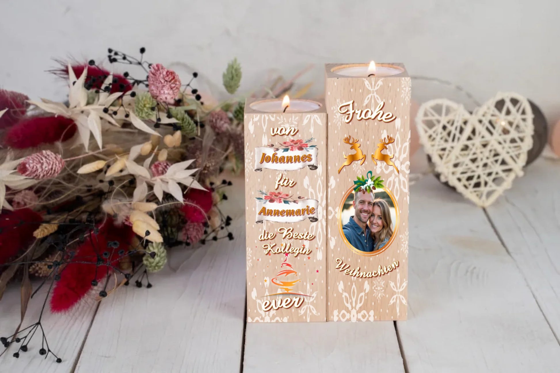 teelichthalter-massiv-holz-2er-set-4,5x4,5cm-12-und-14cm-hoch-personalisiert-mit-foto-und-zwei-namen-weihnachtliches-design-kerzenhalter-rechts-mit-schneeflocken-2-rentier-umrissen-in-gold-ueber-dem-foto-mit-ovalem-goldenem-rahmen-ganz-oben-steht-frohe-und-ganz-unten-steht-weihnachten-design-kerzenhalter-links-schriftzug-von-persnalisierter-name-auf-schriftrolle-fuer-personalisierter-name-die-beste-kollegin-ever-teelichthalter-steht-auf-weißem-tisch-im-hintergrund-liegt-ein-strauss-aus-trockenblumen