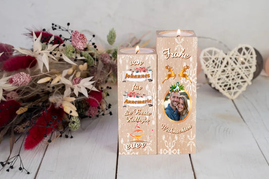 teelichthalter-massiv-holz-2er-set-4,5x4,5cm-12-und-14cm-hoch-personalisiert-mit-foto-und-zwei-namen-weihnachtliches-design-kerzenhalter-rechts-mit-schneeflocken-2-rentier-umrissen-in-gold-ueber-dem-foto-mit-ovalem-goldenem-rahmen-ganz-oben-steht-frohe-und-ganz-unten-steht-weihnachten-design-kerzenhalter-links-schriftzug-von-persnalisierter-name-auf-schriftrolle-fuer-personalisierter-name-die-beste-kollegin-ever-teelichthalter-steht-auf-weißem-tisch-im-hintergrund-liegt-ein-strauss-aus-trockenblumen