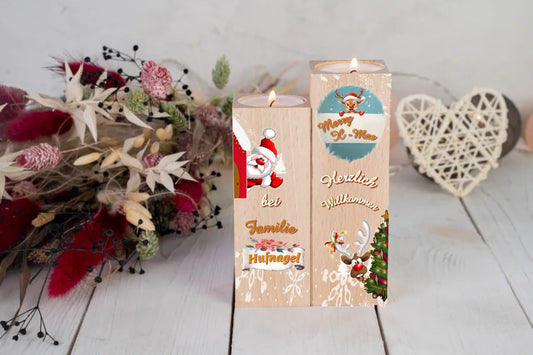 teelichthalter-massiv-holz-2er-set-4,5x4,5cm-12-und-14cm-hoch-personalisiert-mit-familiennamen-weihnachtliches-design-im-comic-style-kerzenhalter-rechts-mit-schneeflocken-oben-ein-rentier-mit-banner-und-schriftzug-merry-x-mas-darunter-schriftzug-herzlich-willkommen-und-ganz-unten-ein-lustiges-rentier-schaut-hinter-weihnachtsbaum-hervor-kerzenhalter-links-oben-winkt-ein-weihnachtsmann-darunter-der schriftzug-bei-familie-personalisierter-familienname-teelichthalter-auf-tisch-dahinter-trockenblumen
