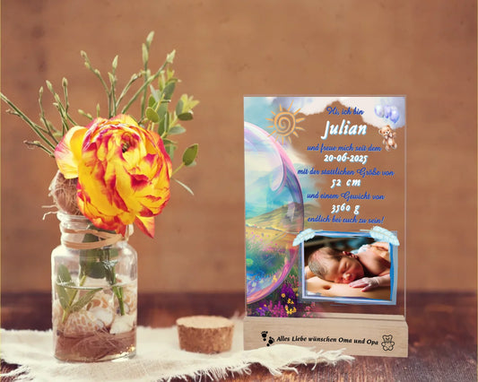 acrylglas-fotoaufsteller-15x20cm-mit-graviertem-standfuß-aus-holz-personalisierter-steckbrief-mit-geburtsdaten-und-foto-hauptfarbe-des-designs-blau-und-pasteltoene-standfuss-mit-wunschtext-graviert-fotoauftseller-steht-auf-rustikalem-holztisch-neben-einer-rose