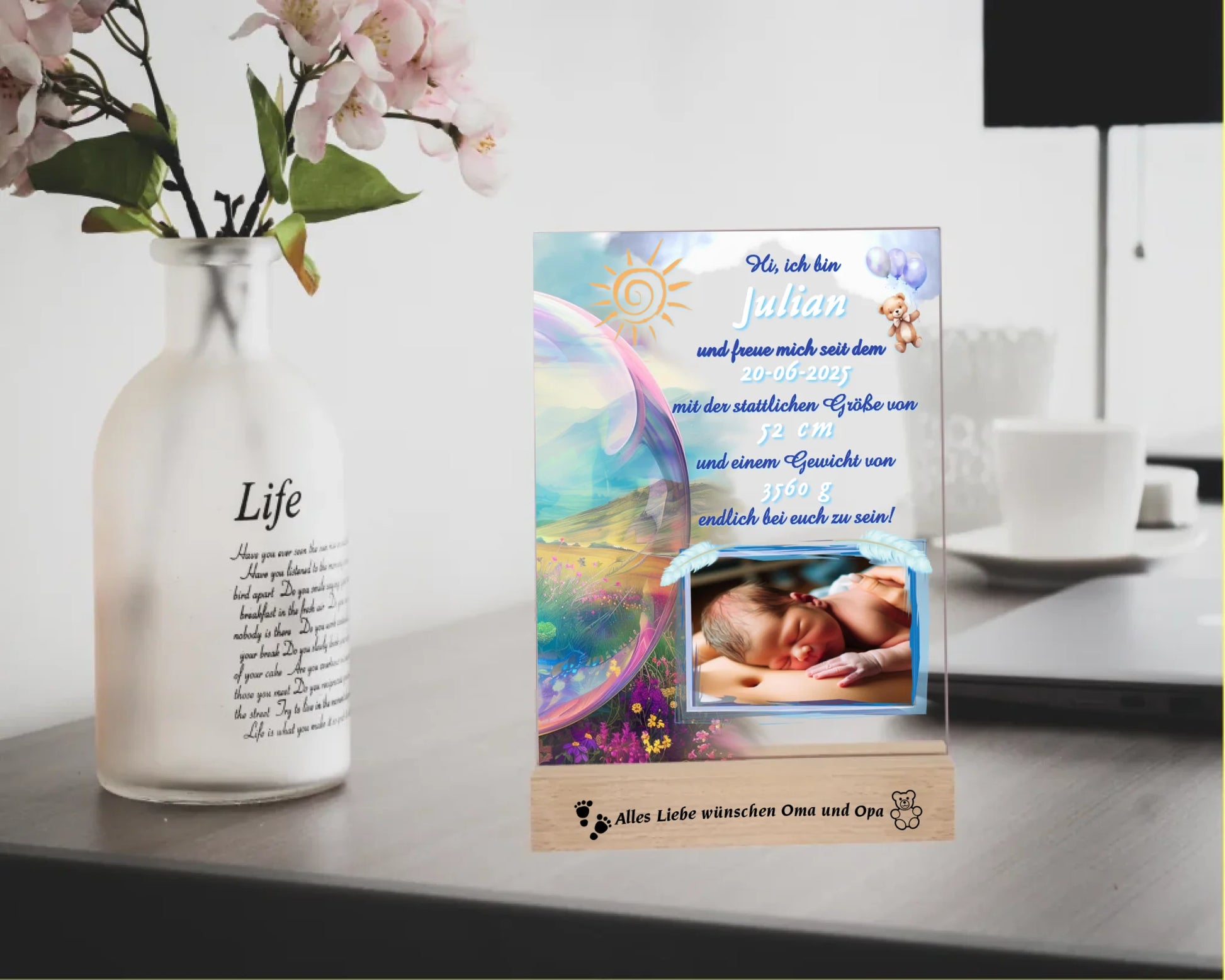 acrylglas-fotoaufsteller-15x20cm-mit-graviertem-standfuß-aus-holz-personalisierter-steckbrief-mit-geburtsdaten-und-foto-hauptfarbe-des-designs-blau-und-pasteltoene-standfuss-mit-wunschtext-graviert-fotoauftseller-steht-auf-schreibtisch-neben-vase-mit-blumen