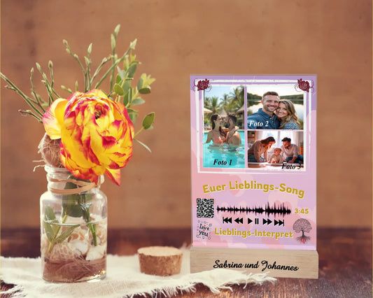 acrylglas-15x20cm-mit-graviertem-standfuss-aus-echtholz-acrylglas-mit-3-fotos-und-ausgewähltem-songtitel-und-interpret-mit-qr-code-design-hintergrund-pastell-rosa-in-verschiedenen-farbtoenen-standfss-graviert-mit-namen-oder-wunschtext-acrylaufsteller-steht-auf-rustikalem-holztisch-neben-einer-rose