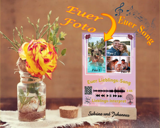 acrylglas-15x20cm-mit-graviertem-standfuss-aus-echtholz-wichtelgeschenk-mit-hinweis-zu-personalisierung-acrylglas-mit-3-fotos-und-ausgewähltem-songtitel-und-interpret-mit-qr-code-design-hintergrund-pastell-rosa-in-verschiedenen-farbtoenen-standfss-graviert-mit-namen-oder-wunschtext-acrylaufsteller-steht-auf-rustikalem-holztisch-neben-einer-rose