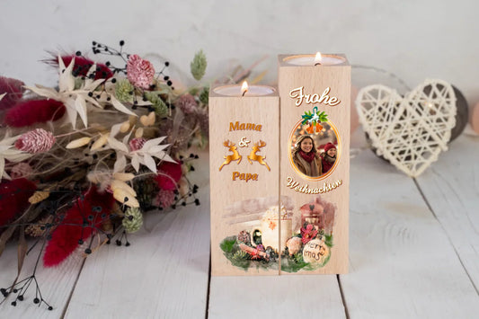teelichthalter-massiv-holz-2er-set-4,5x4,5cm-12-und-14cm-hoch-personalisiert-mit-foto-und-zwei-namen-weihnachtliches-design-mit-schriftzug-frohe-ueber-dem-foto-mit-ovalem-goldenem-rahmen-darunter-schriftzug-weihnachten-design-kerzenhalter-links-die-beiden-personalisierten-namen-beispiel-mama-papa-in-dunklem-orange-dazwischen-zwei-umrisse-von-rentieren-in-gold-ganz-unten-erstreckt-sich-motiv-weihnachtsgedeck-ueber-beide-kerzenhalter-in-aquqrell-optik-teelichthalter-vor-roten-trockenblumen