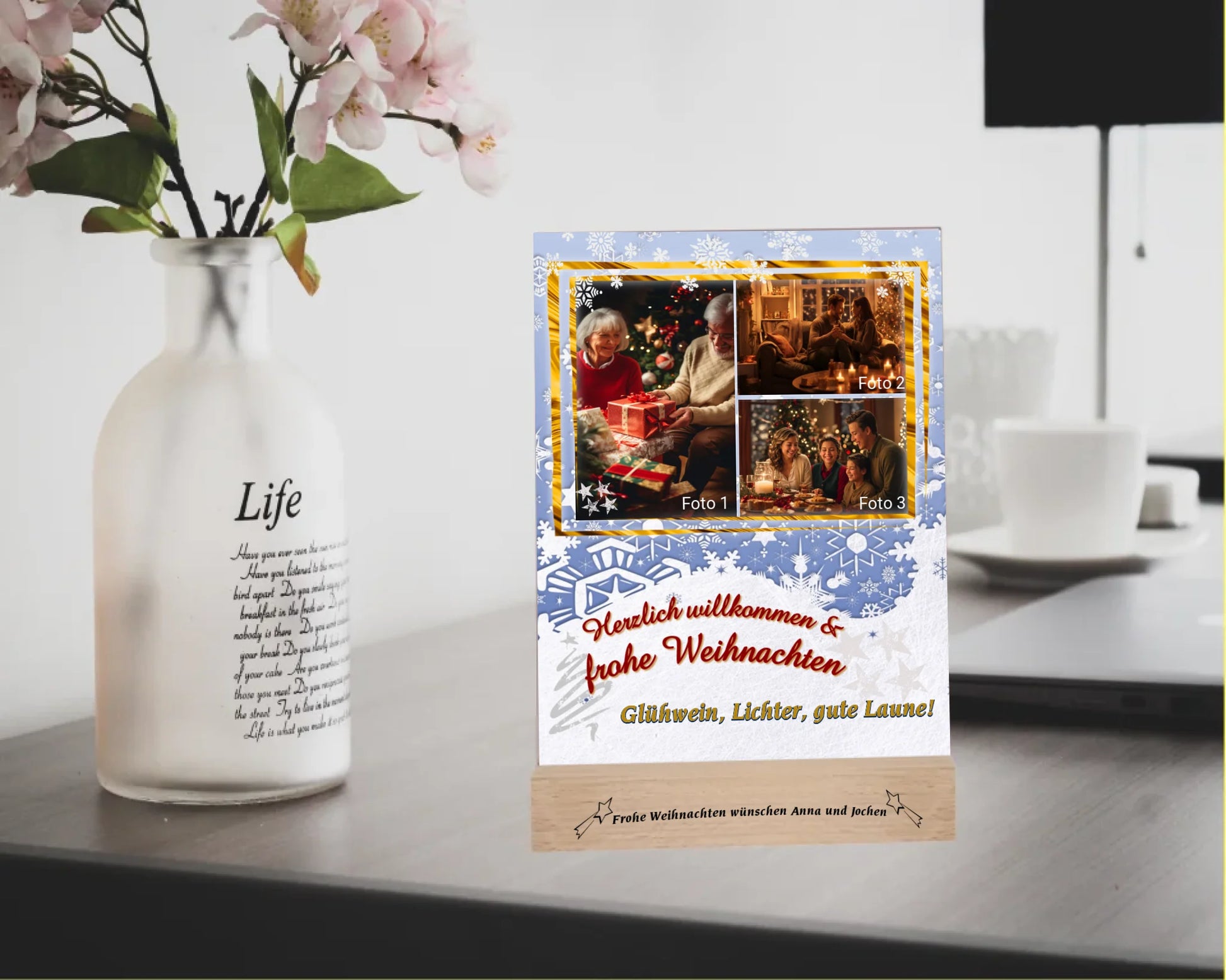 acrylglas-15x20cm-mit-graviertem-standfuss-aus-echtholz-acrylglas-ist-personalisiert-mit-3-fotos-und-einem-aus-5-spruechen-hintergrundfarbe-weiß-hellblau-mit-schneeflocken-der fotoaufsteller-steht-auf-einem-schreibtisch-neben-einer-vase-mit-blumen