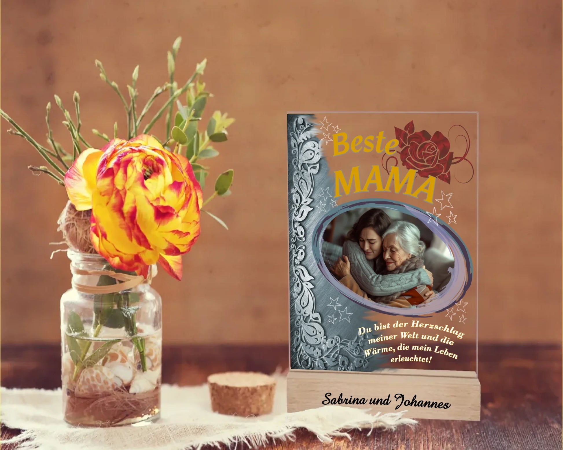 fotoaufsteller-15x20cm-aus-acryl-mit-echtholzsockel-mit-personalisierbaren-foto-silbernen-akzent-auf-der-linken-seite-und-einem-goldgelben-lebensbaum-über-dem-foto-steht-beste-mama-unter-dem-foto-steht-einer-der-fünf-wählbaren-sprüche-der-aufsteller-steht-auf-einem-holztisch-daneben-eine-rose