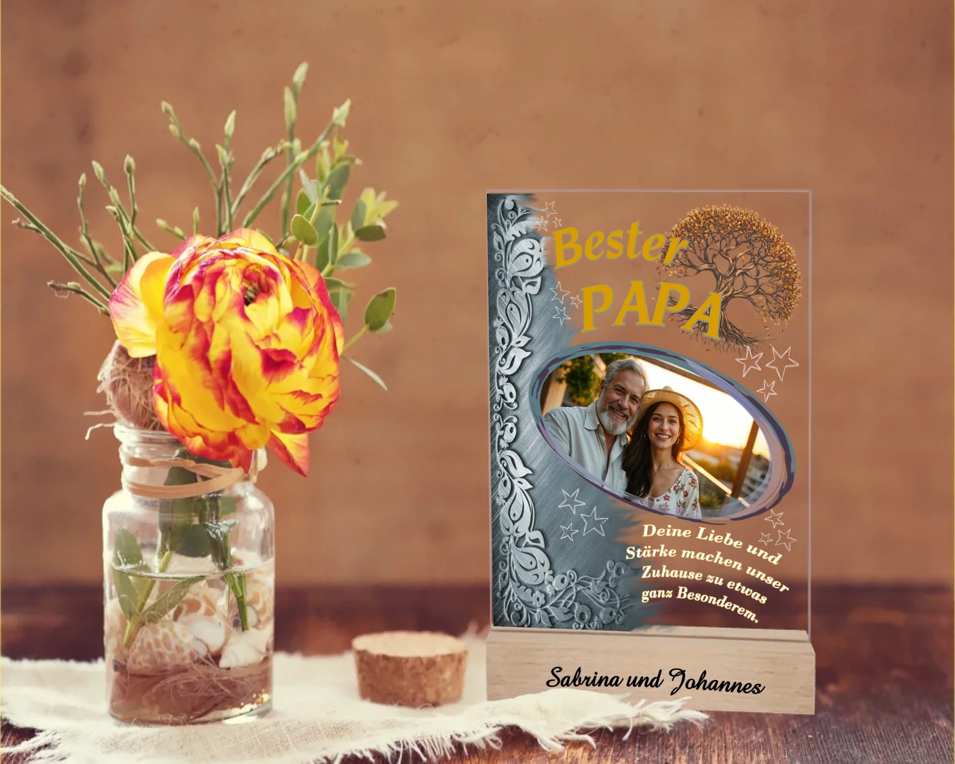 fotoaufsteller-aus-acryl-mit-echtholzsockel-mit-personalisierbaren-foto-silbernen-akzent-auf-der-linken-seite-und-einem-goldgelben-lebensbaum-über-dem-foto-steht-bester-papa-unter-dem-foto-steht-einer-der-fünf-wählbaren-sprüche-der-aufsteller-steht-auf-einem-holztisch-daneben-eine-rose