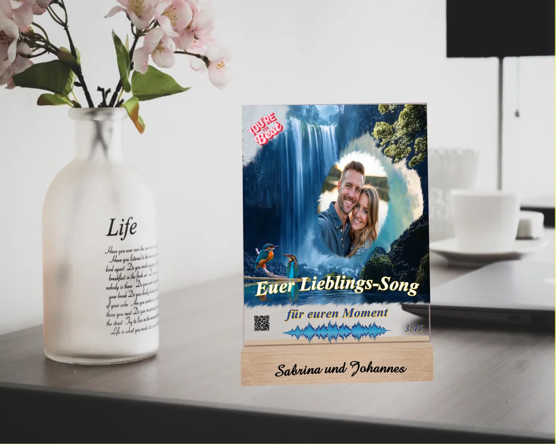 acrylaufsteller-15x20cm-personalisiert-mit-foto-titel-und-interpret-des-ausgewählten-songs-mit-qr-code-und-gravierten-namen-am-holzsockel-design-hintergrund-ein-wasserfall-in-strahlendem-blau-fotoaufsteller-steht-auf-einem-schreibtisch
