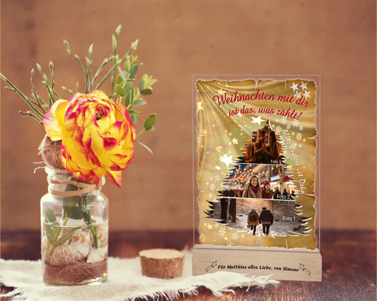 fotoaufsteller-acryl-15x20cm-mit-graviertem-standfuss-geschenkidee-papa-acrylglas-mit-3-teiliger-foto-collage-in-tannenbaum-form-darueber-schriftzug-weihnachten-mit-dir-ist-das-was-zaehlt-und-neben-der-collage-steht-alles-andere-ist-deko-mit-einem-hintergrund-optik-goldenes-papier-mit-sternen-und-schneeflocken-fotoaufsteller-steht-auf-holztisch-neben-einer-rose