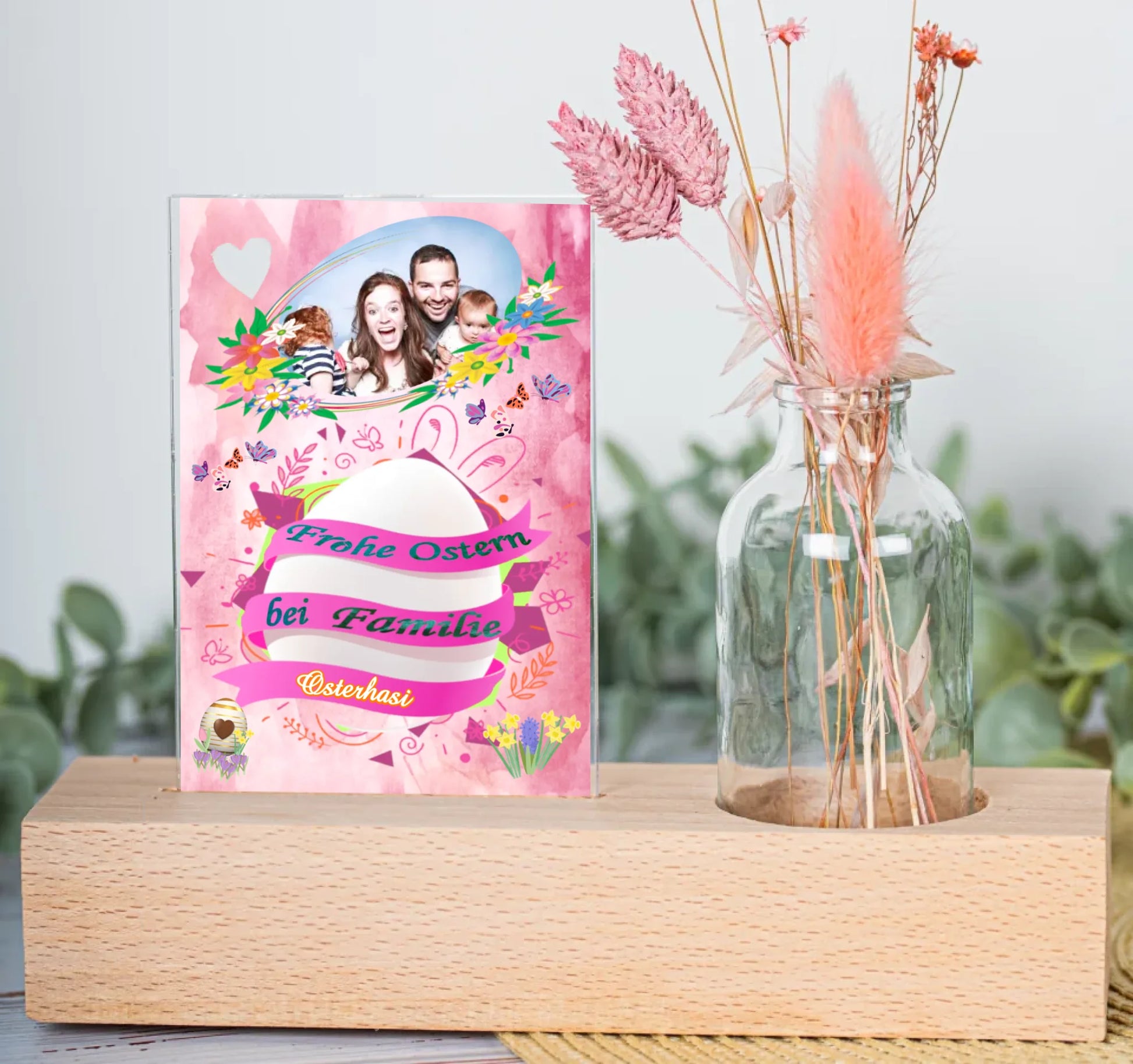 farbenfrohes-motiv-hauptsächlich-in-pink-mit-großem-osterei-umwickelt-mit-banner-mit-schriftzug-frohe-ostern-bei-familie-...-darüber-ein-familienfoto