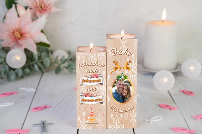 teelichthalter-massiv-holz-2er-set-4,5x4,5cm-12-und-14cm-hoch-personalisiert-mit-foto-und-zwei-namen-weihnachtliches-design-kerzenhalter-rechts-mit-schneeflocken-2-rentier-umrissen-in-gold-ueber-dem-foto-mit-ovalem-goldenem-rahmen-ganz-oben-steht-frohe-und-ganz-unten-steht-weihnachten-design-kerzenhalter-links-schriftzug-wuenschen-euch-dann-die-persnalisierten-namen-auf-schriftrolle-teelichthalter-steht-auf-weißem-tisch-im-hintergrund-steht-eine-weiße-kerze-neben-rosa-lilien